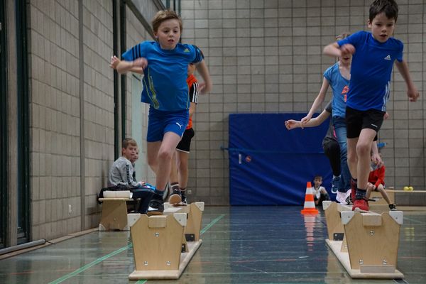 Kinder laufen in der Sporthalle über eine umgedrehte Bank 